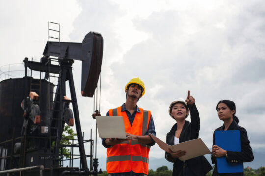 engineering-team-stands-beside-working-oil-pumps-with-sky